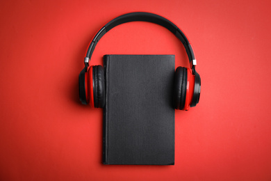 Book and modern headphones on red background, top view