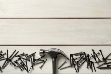 Hammer and metal nails on white wooden table, flat lay. Space for text