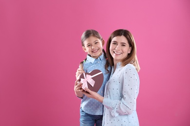 Happy mother and daughter with gift on color background. International Women's Day