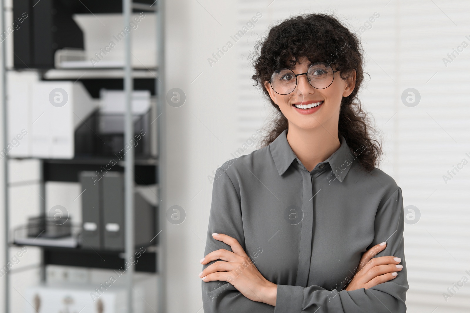 Photo of Portrait of confident businesswoman with crossed arms indoors. Beautiful lady in glasses smiling and looking into camera. Space for text