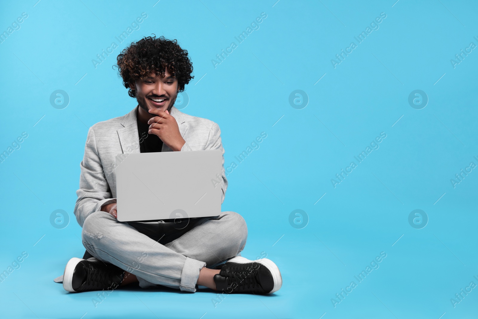 Photo of Smiling man with laptop on light blue background, space for text