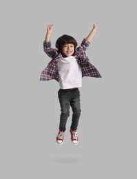 Happy boy jumping on grey background, full length portrait