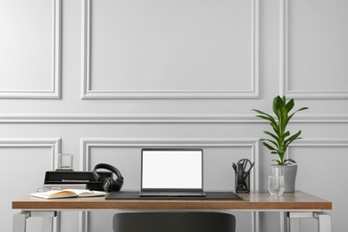 Photo of Stylish workplace with laptop, houseplant and stationery on wooden table near light grey wall