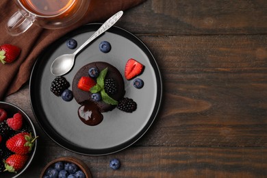 Plate with delicious chocolate fondant, berries and mint on wooden table, flat lay. Space for text