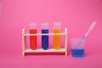 Photo of Beaker and test tubes with colorful liquids in wooden stand on bright pink background. Kids chemical experiment set