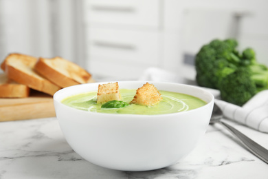 Photo of Delicious broccoli cream soup with croutons served on white marble table