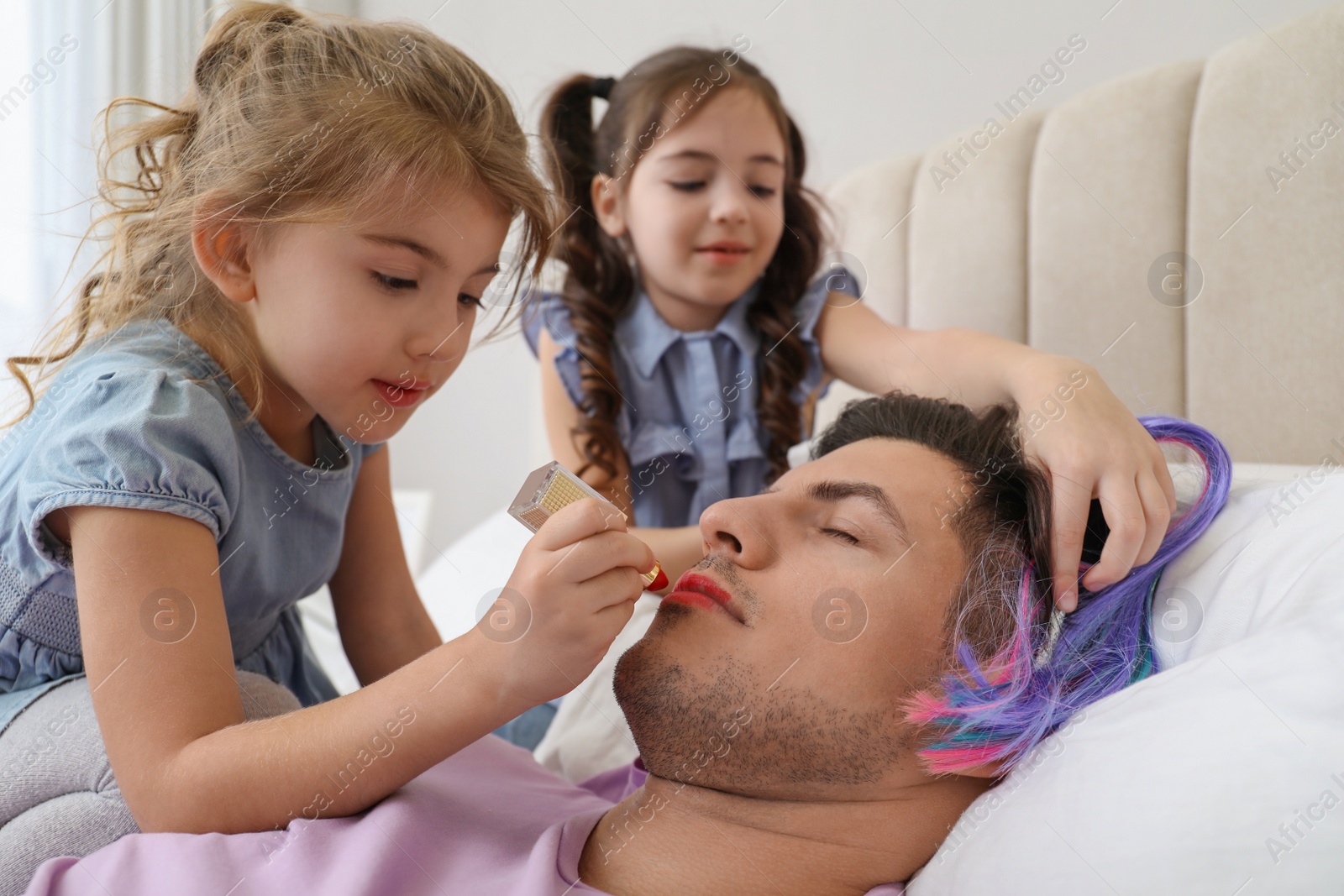 Photo of Cute little children painting face of their father while he sleeping in bed at home