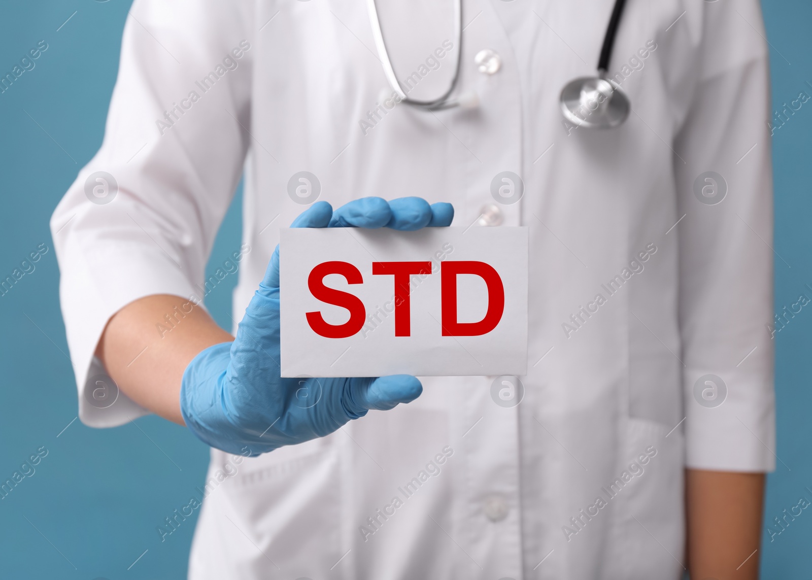 Photo of Doctor holding sheet of paper with abbreviation STD on light blue background, closeup