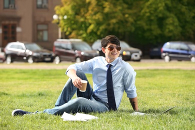 Photo of Young man with cup of coffee sitting on green lawn in park. Joy in moment