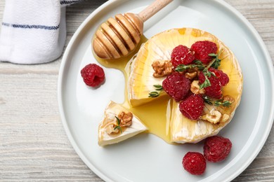 Photo of Brie cheese served with raspberries, walnuts and honey on white wooden table, flat lay
