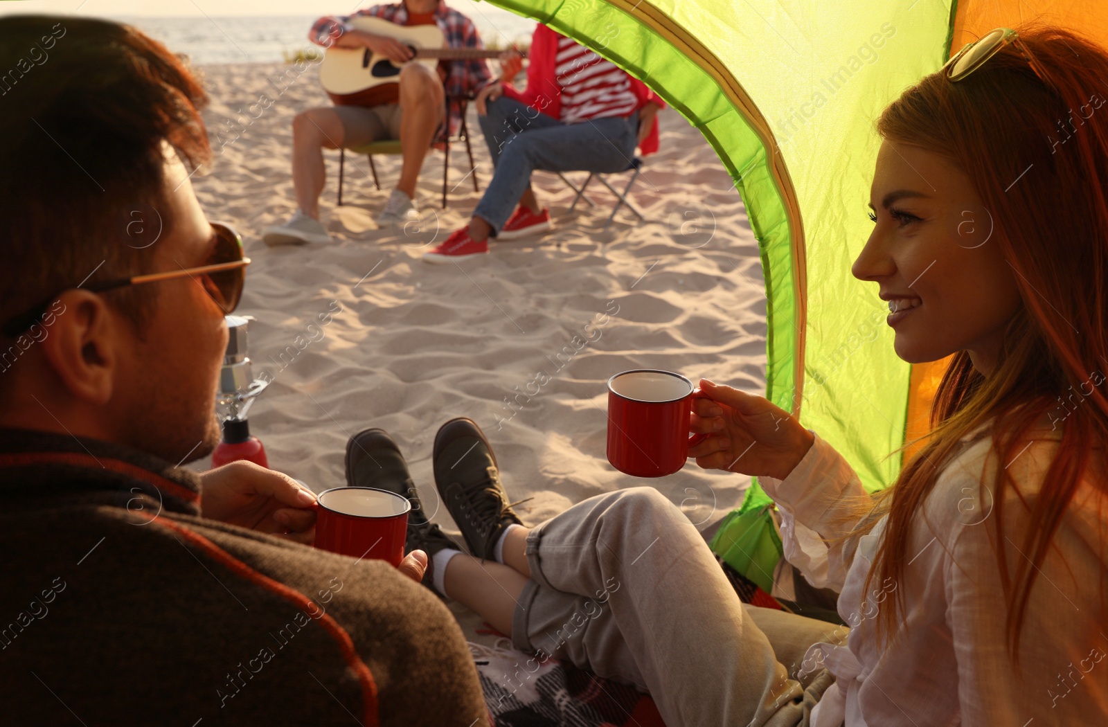 Photo of Friends resting on sandy beach. View from camping tent