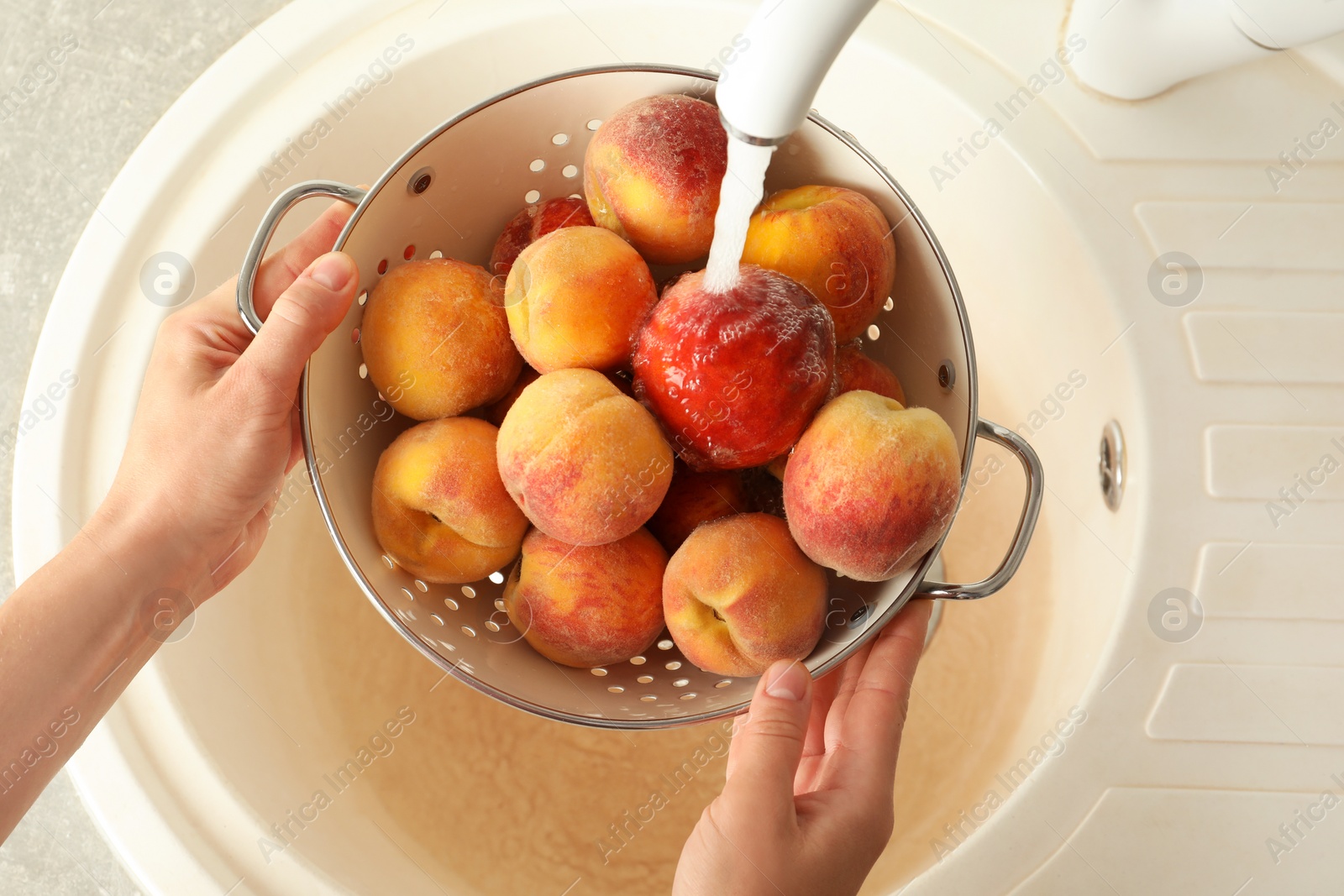 Photo of Woman washing fresh sweet peaches in kitchen