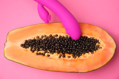 Half of papaya and purple vibrator on pink background, flat lay. Sex concept