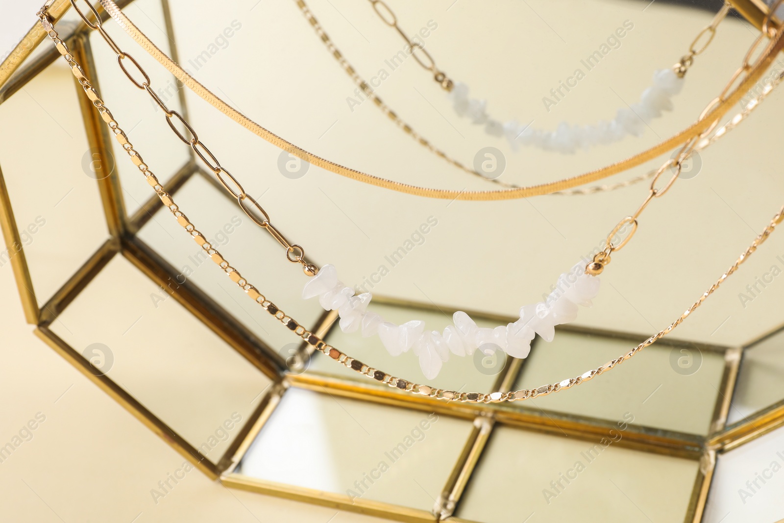 Photo of Stand with different metal chains on beige background, closeup. Luxury jewelry