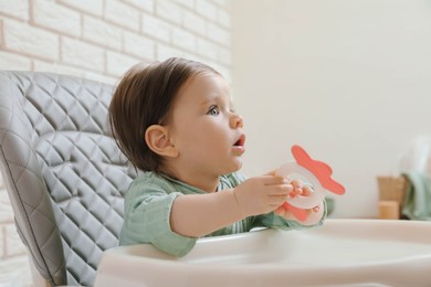 Photo of Cute little baby with teether in high chair indoors