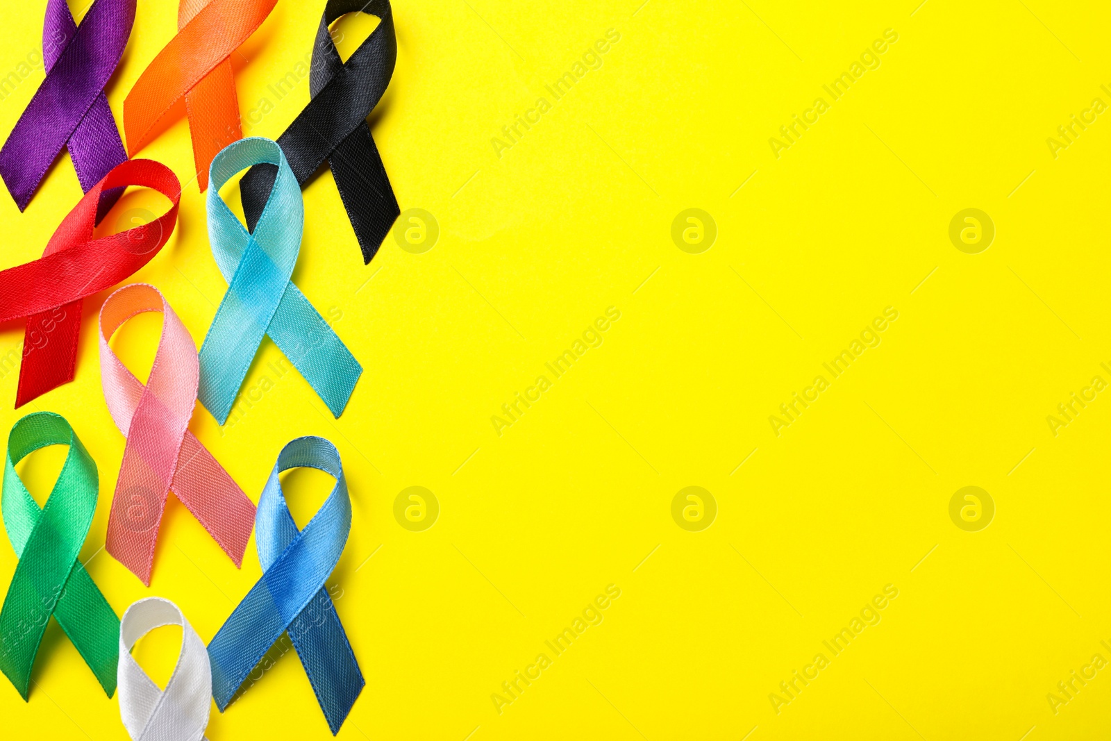 Photo of Colorful ribbons on yellow background, flat lay with space for text. World Cancer Day