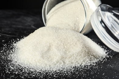 Photo of Overturned bowl with granulated sugar on black table, closeup