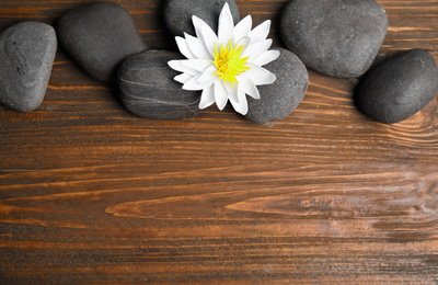 Photo of Stones with lotus flower and space for text on wooden background, flat lay. Zen lifestyle