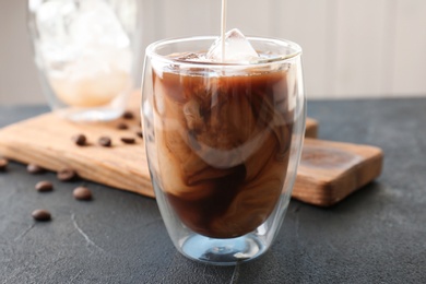 Photo of Pouring milk into glass with cold brew coffee on table