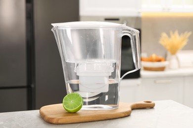 Photo of Water filter jug and lime on light table in kitchen, closeup