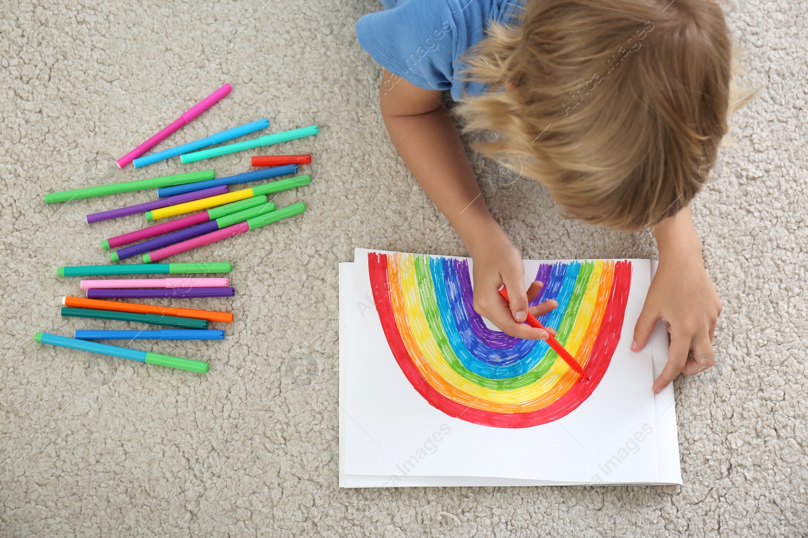 Photo of Little boy drawing rainbow on floor indoors, above view. Stay at home concept