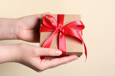 Photo of Woman holding gift box with red bow on beige background, closeup