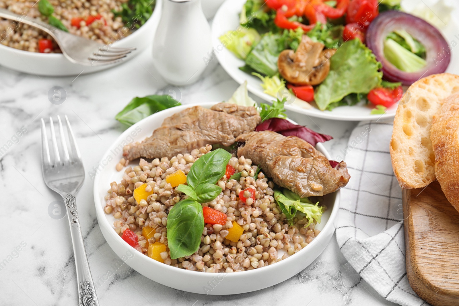 Photo of Tasty buckwheat porridge with meat on white marble table