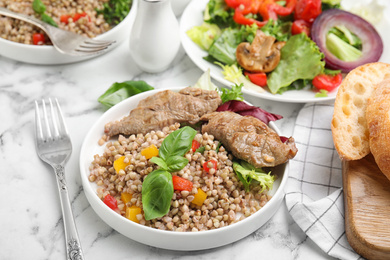 Photo of Tasty buckwheat porridge with meat on white marble table