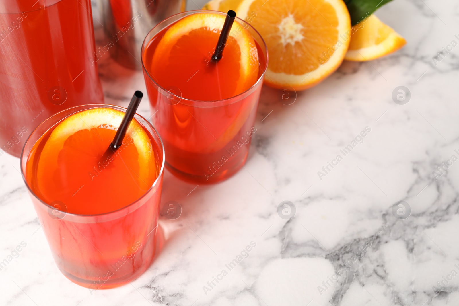 Photo of Aperol spritz cocktail, orange slices and straws in glasses on white marble table, closeup. Space for text