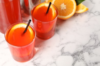 Aperol spritz cocktail, orange slices and straws in glasses on white marble table, closeup. Space for text