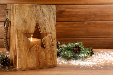 Photo of Christmas lantern with burning candle and fir tree branch on wooden background. Space for text