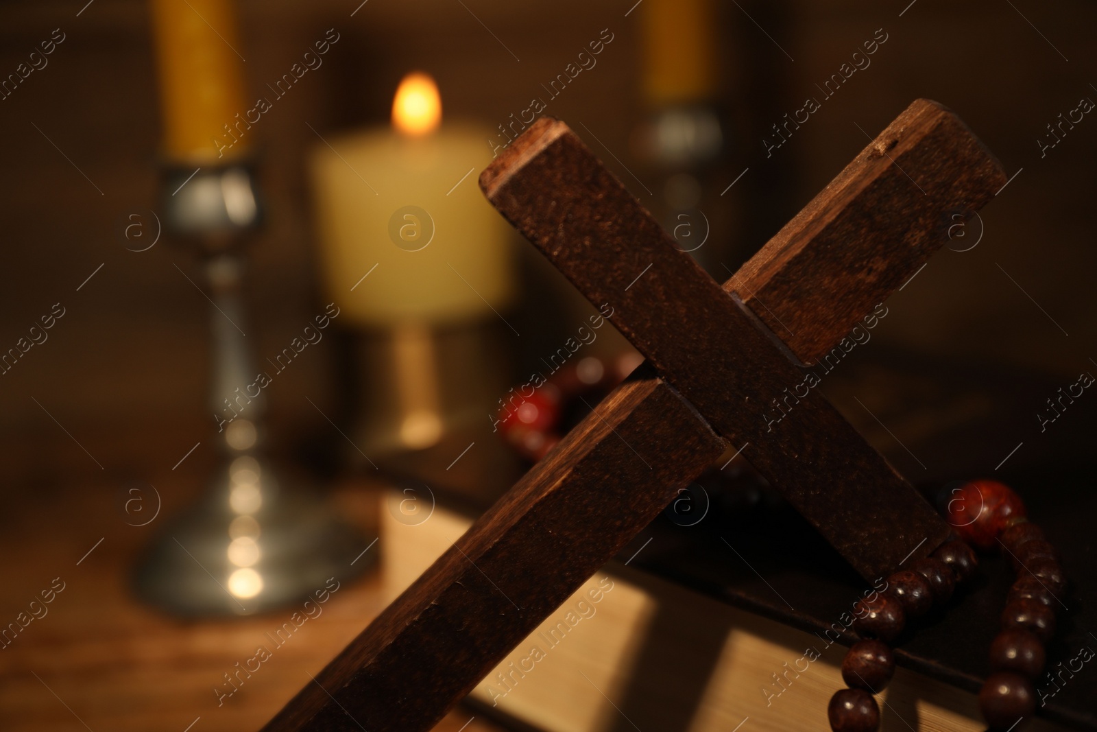 Photo of Wooden cross, Bible, rosary beads and church candles on table, closeup. Space for text