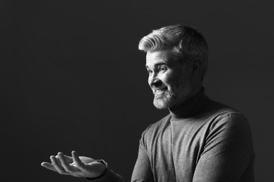 Photo of Portrait of smiling man gesturing on dark background. Black and white effect