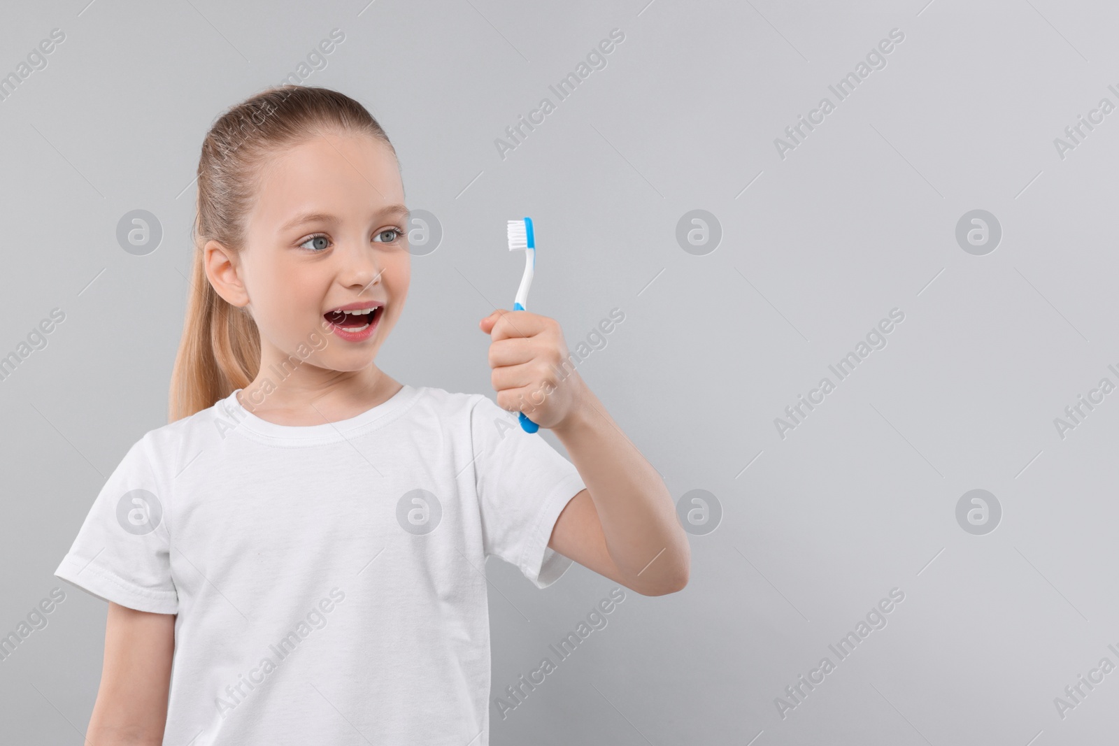 Photo of Happy girl holding toothbrush on light grey background. Space for text