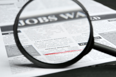 Looking through magnifying glass at newspaper, closeup. Job search concept