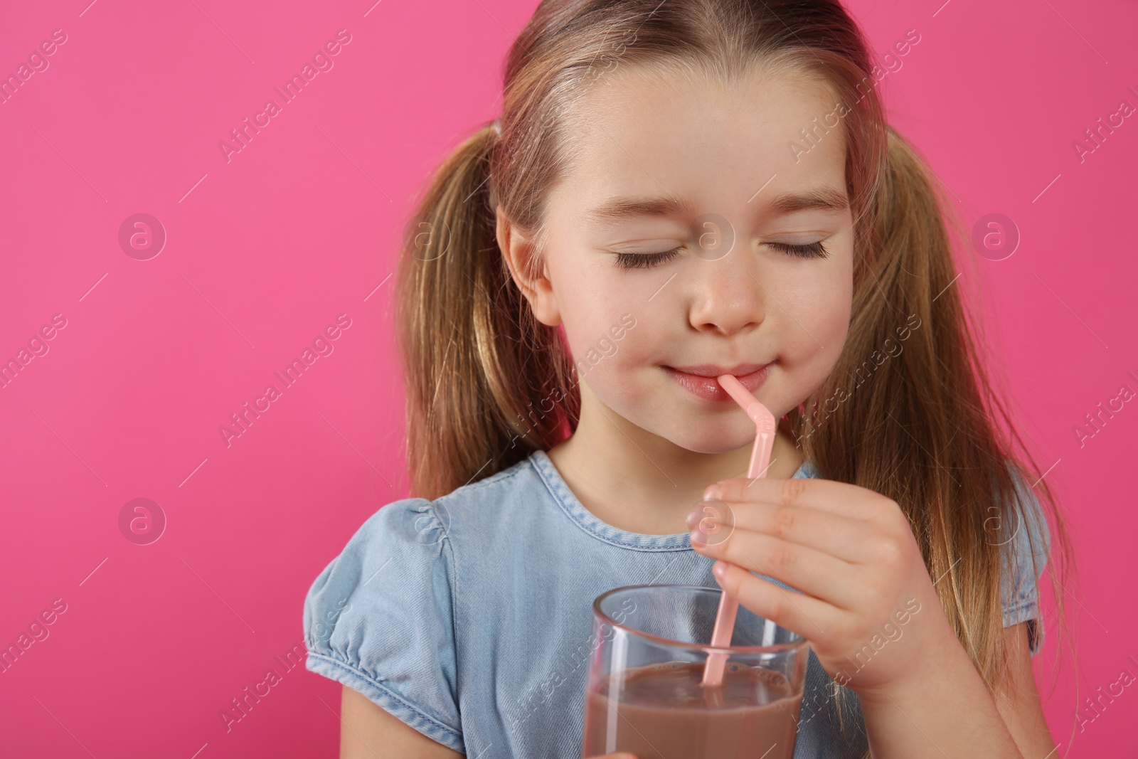 Photo of Cute little child drinking tasty chocolate milk on pink background. Space for text