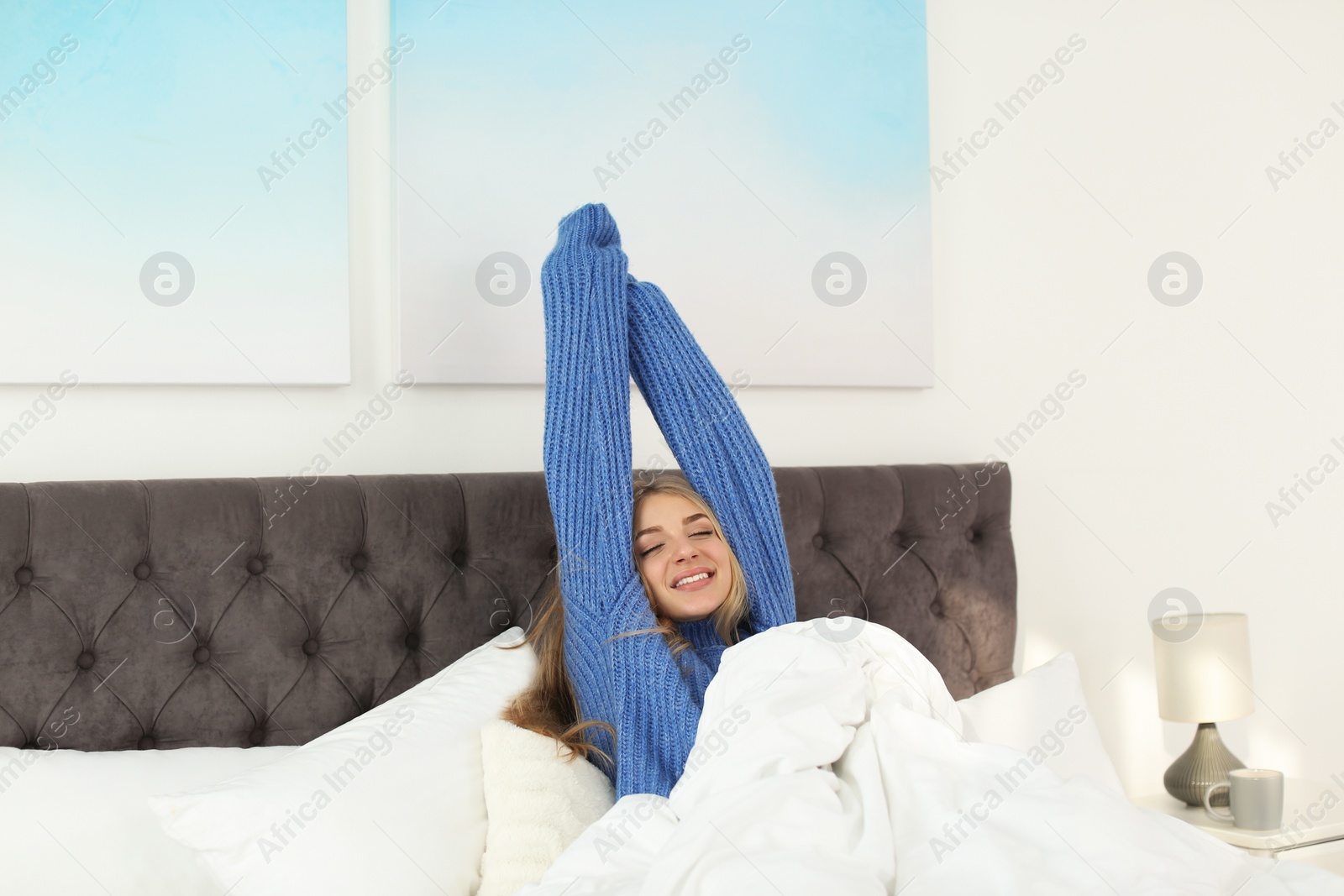 Photo of Beautiful young woman stretching in bed and smiling at home. Winter atmosphere