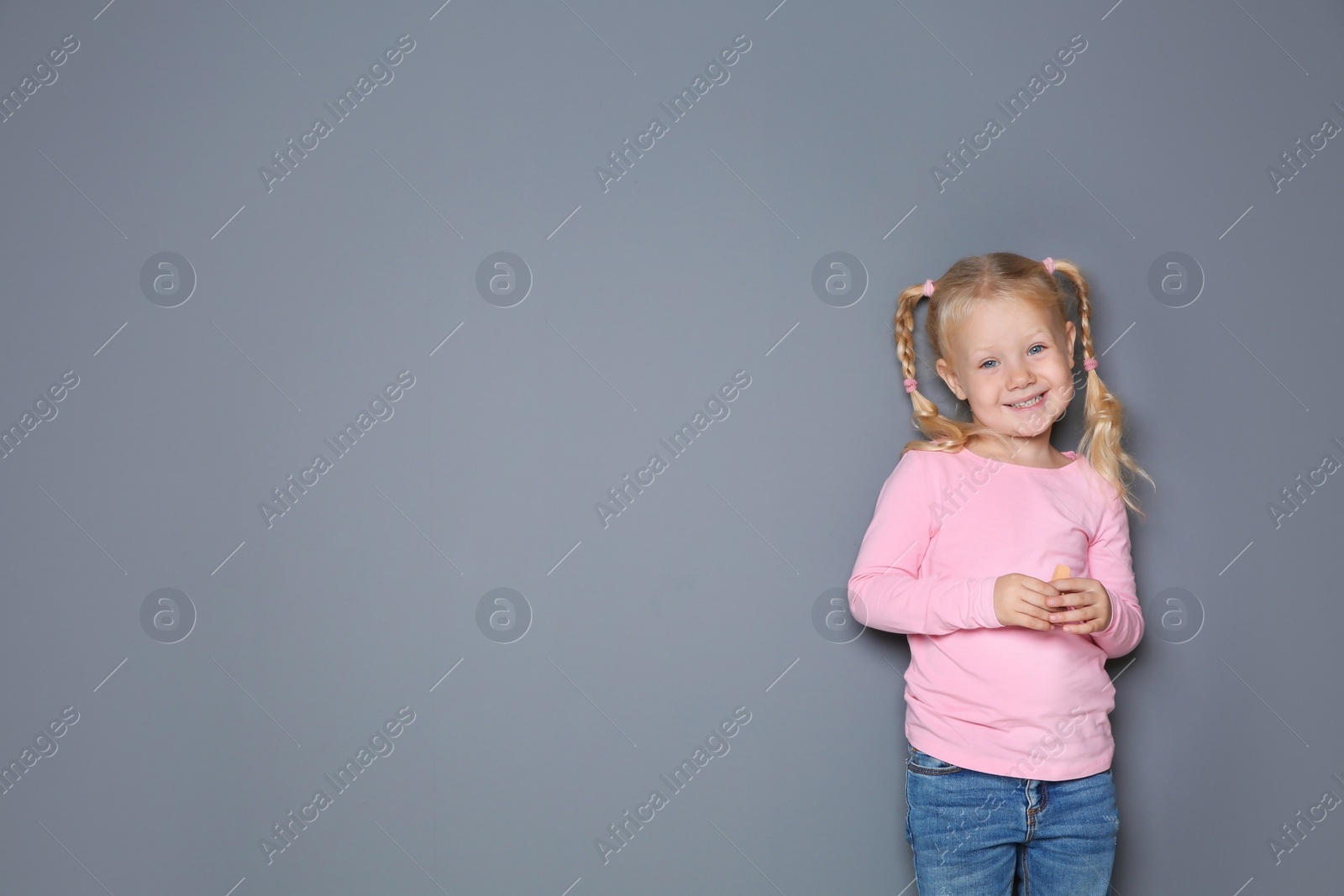 Photo of Little girl with colorful chalk standing against gray background. Space for design