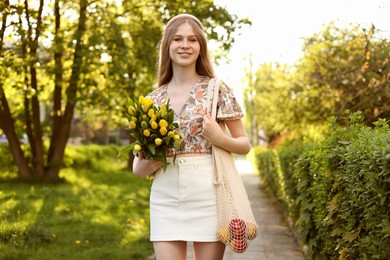 Photo of Beautiful teenage girl with bouquet of yellow tulips and apples in park on sunny day