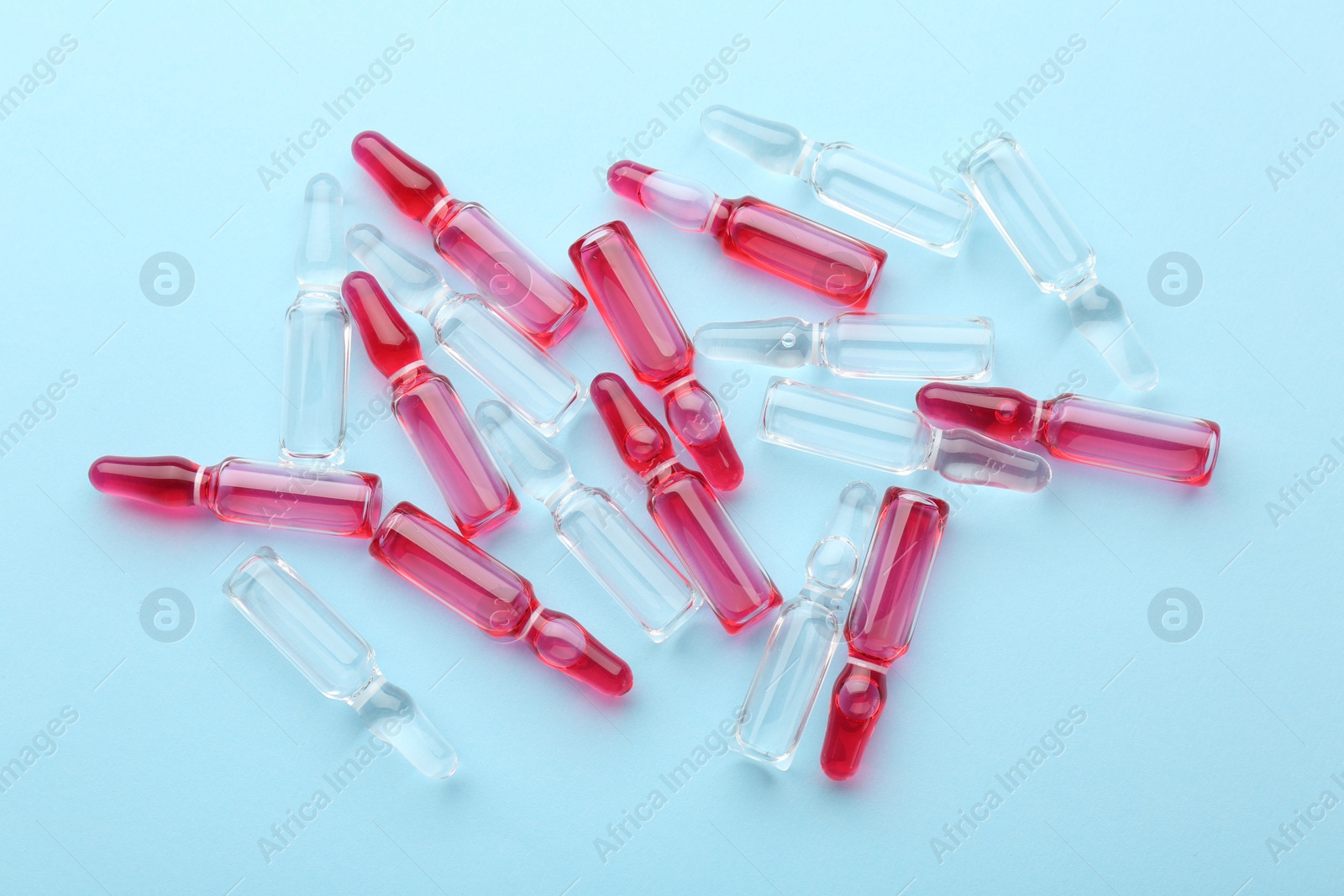 Photo of Glass ampoules with liquid on light blue background, top view