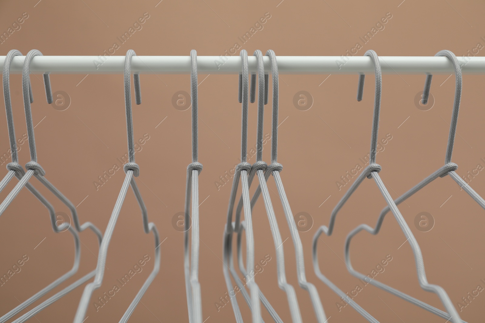 Photo of Empty clothes hangers on rack against light brown background, closeup