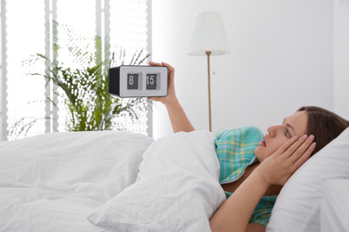 Photo of Sleepy young woman holding clock at home in morning