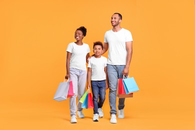 Photo of Family shopping. Happy parents and son with colorful bags on orange background