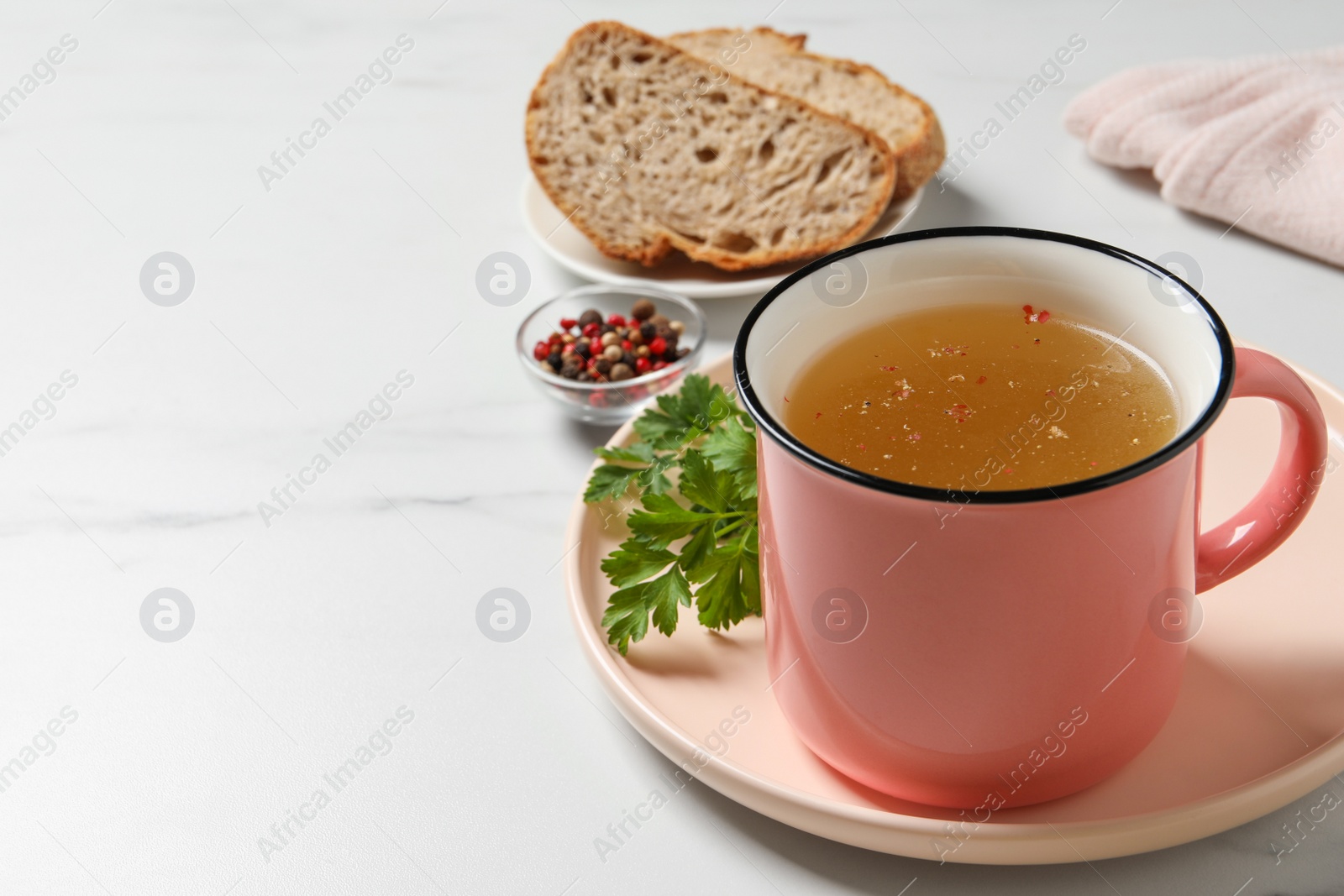 Photo of Hot delicious bouillon in cup on white marble table. Space for text