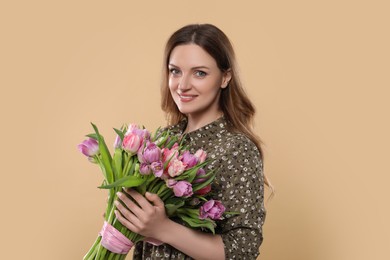 Happy young woman holding bouquet of beautiful tulips on beige background