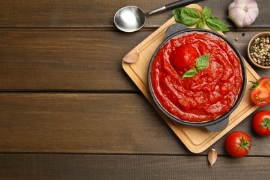 Photo of Homemade tomato sauce in bowl, spoon and ingredients on wooden table, flat lay. Space for text