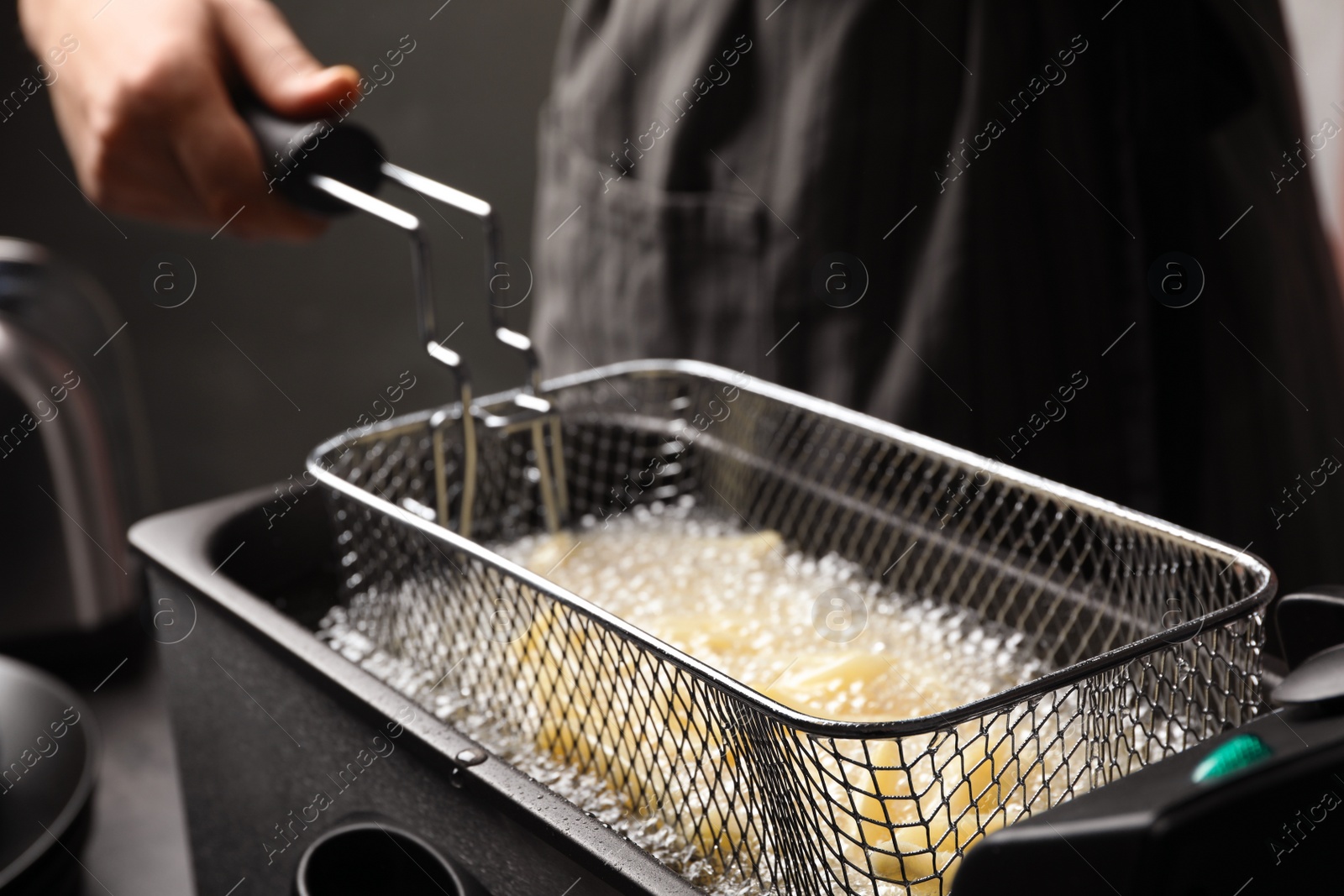 Photo of Chef cooking delicious french fries in hot oil, closeup