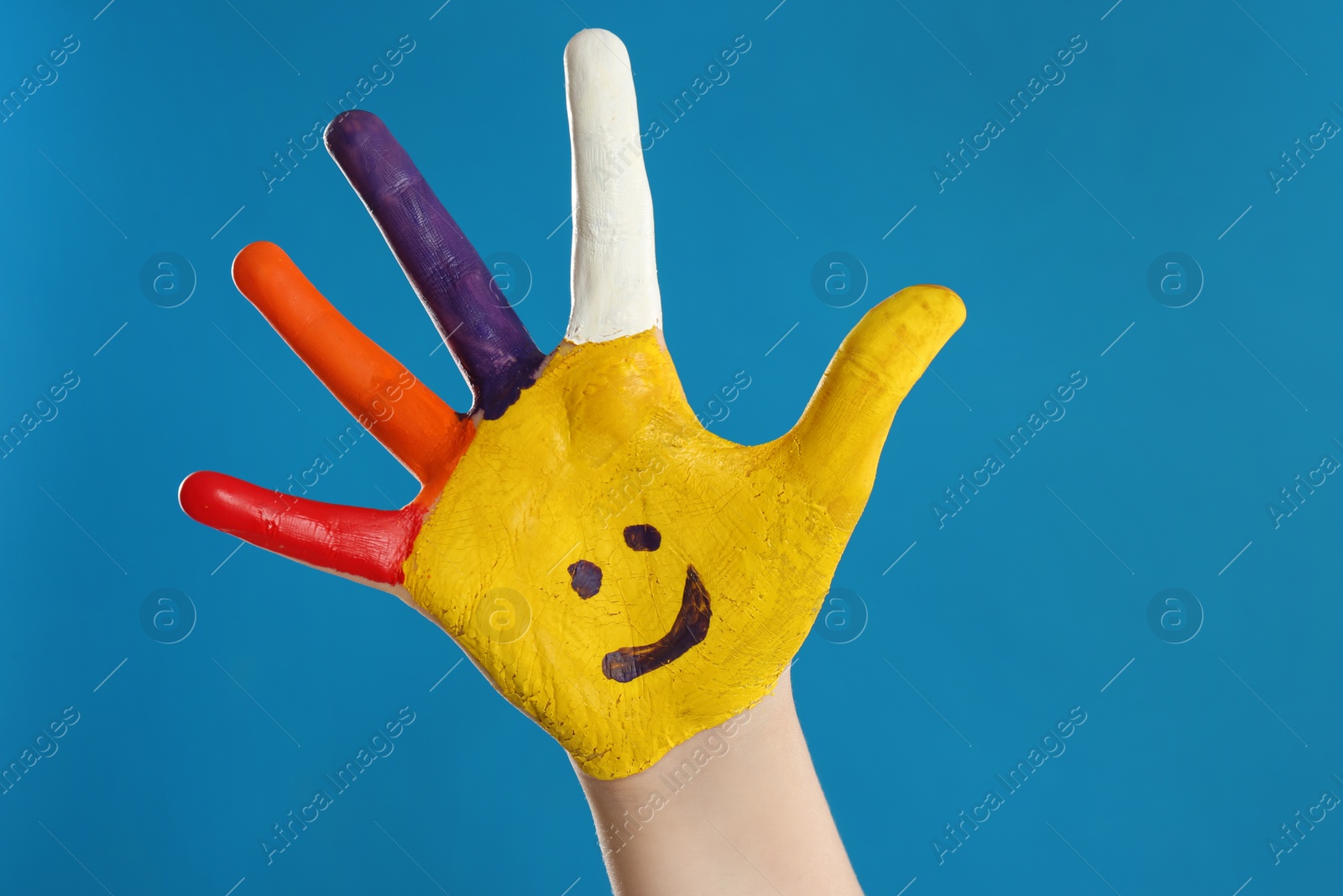 Photo of Kid with smiling face drawn on palm against blue background, closeup