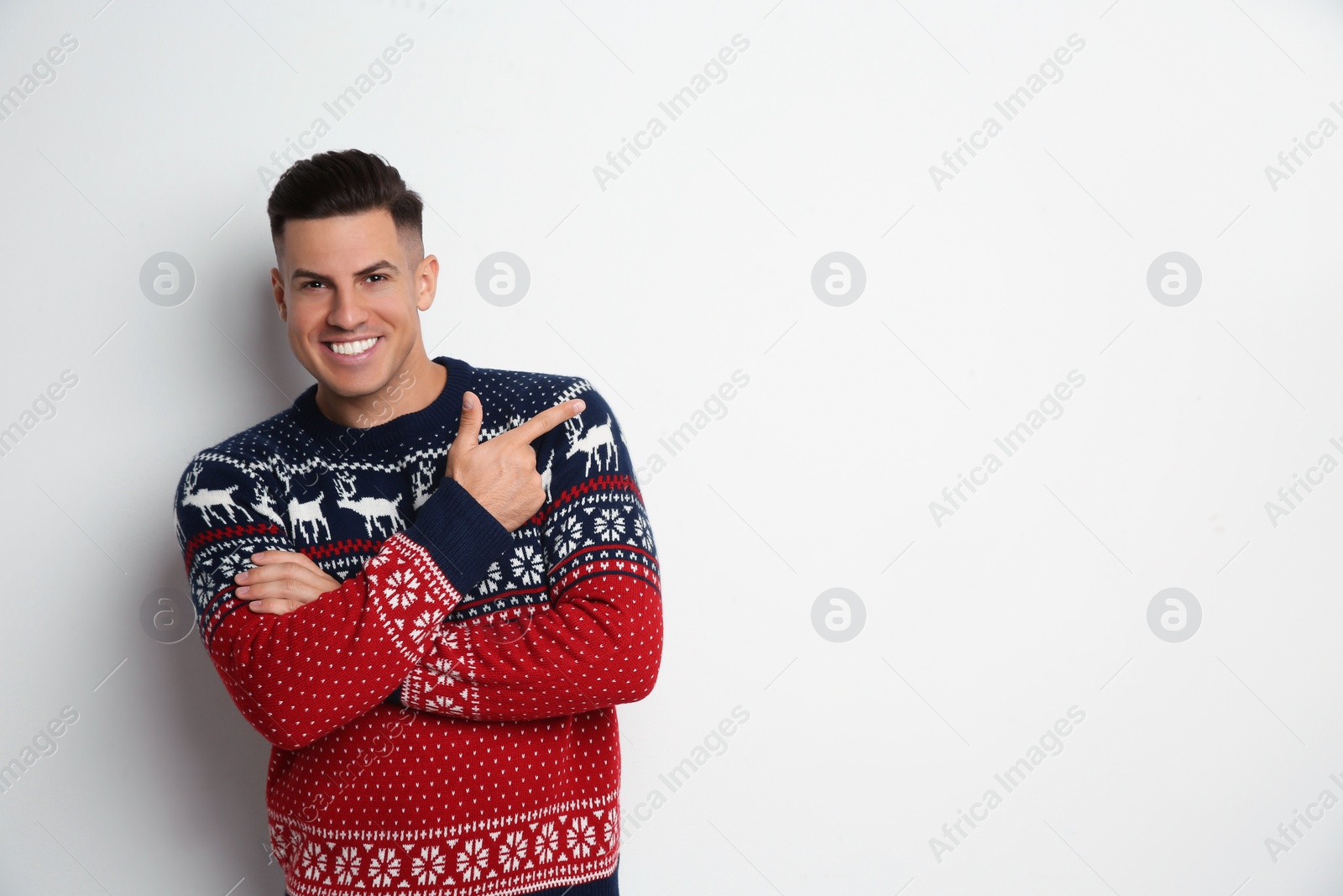 Photo of Handsome man in Christmas sweater pointing on white background, space for text