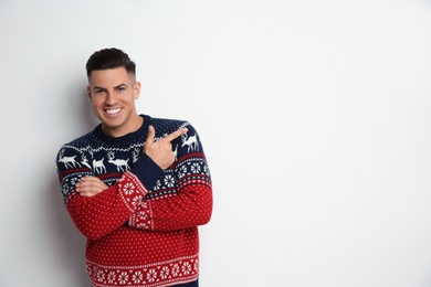 Photo of Handsome man in Christmas sweater pointing on white background, space for text